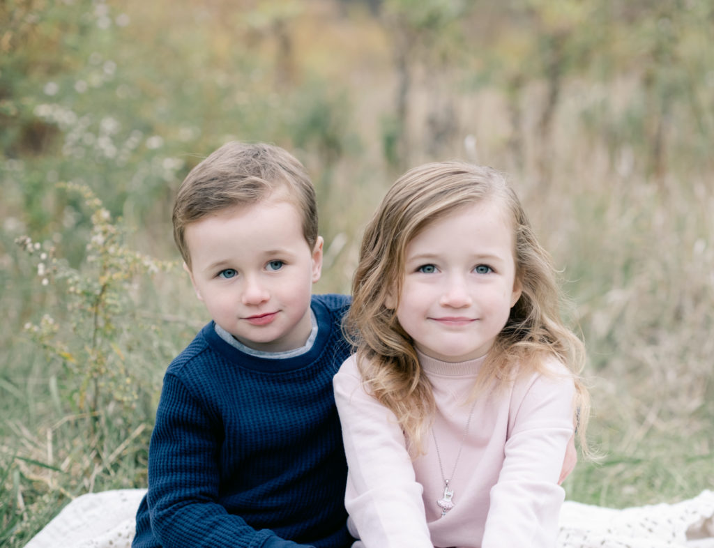 A fall portrait of a brother and sister sitting in a field during their north shore family photographer session