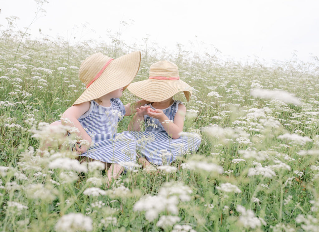 twin girls sitting in field of white flowers brother and sister sitting together