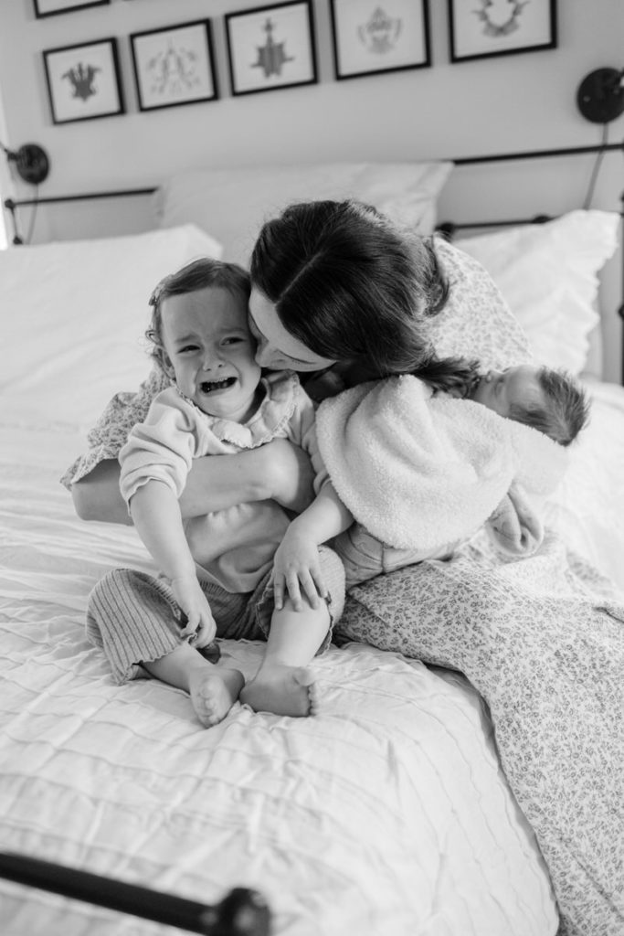 mom kissing toddler and holding newborn baby