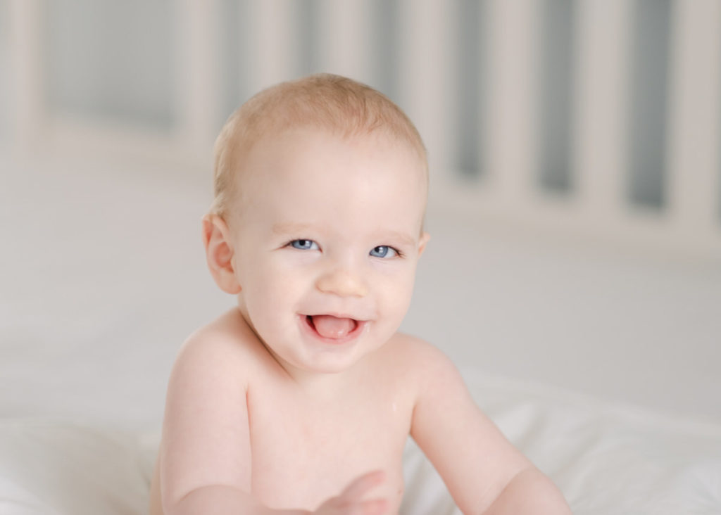 happy smiling six month old sitting on bed