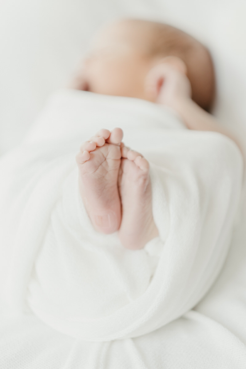 Local Evanston newborn photographer captures an image of a baby wrapped in a white blanket with the focus on the newborn's feet.