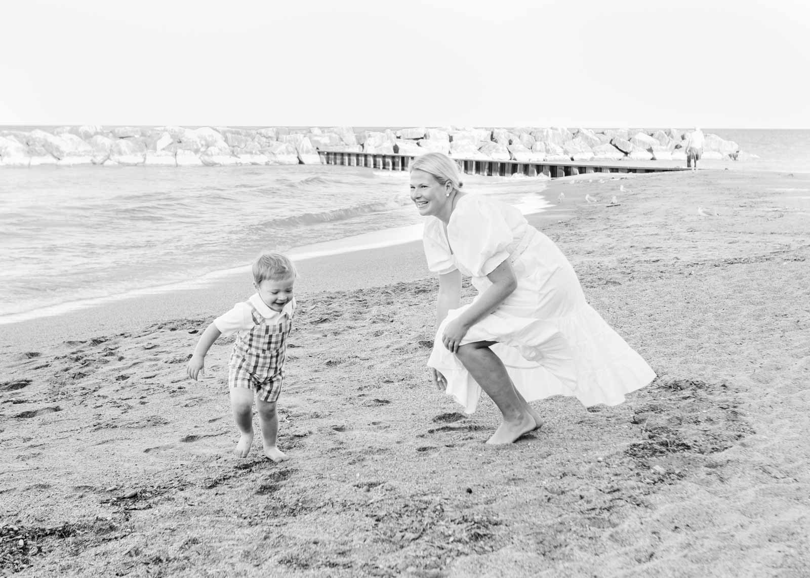 a black and white image of a mom chasing her toddler down lake forest beach