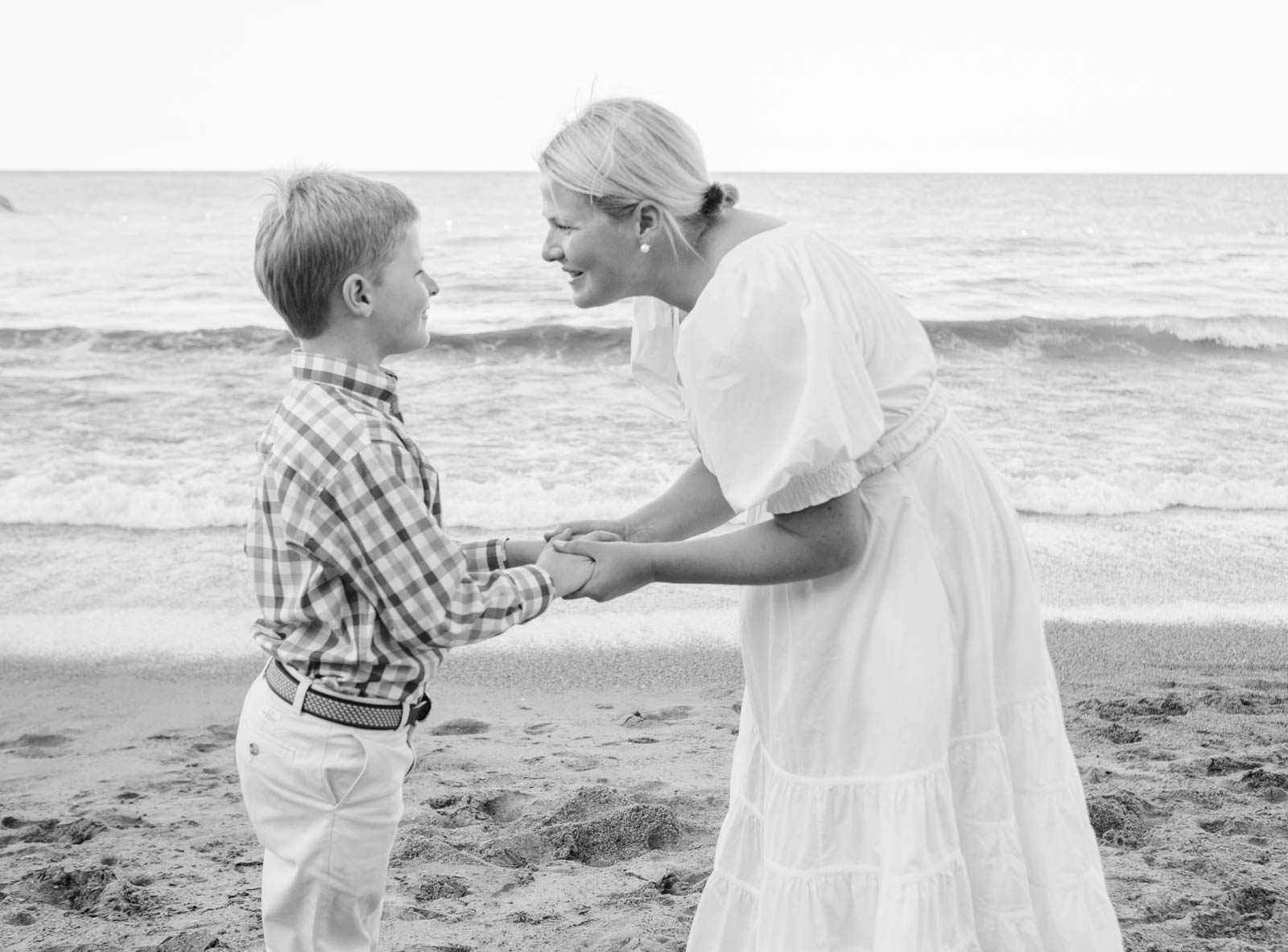 A wilmette photographer captures an image of a mom and son holding hands on the beach looking at each other.