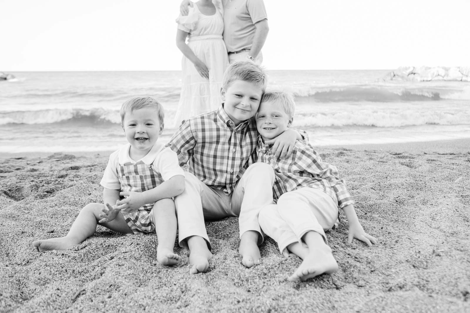 black and white image of three brothers sitting on the beach in front of their parents. 