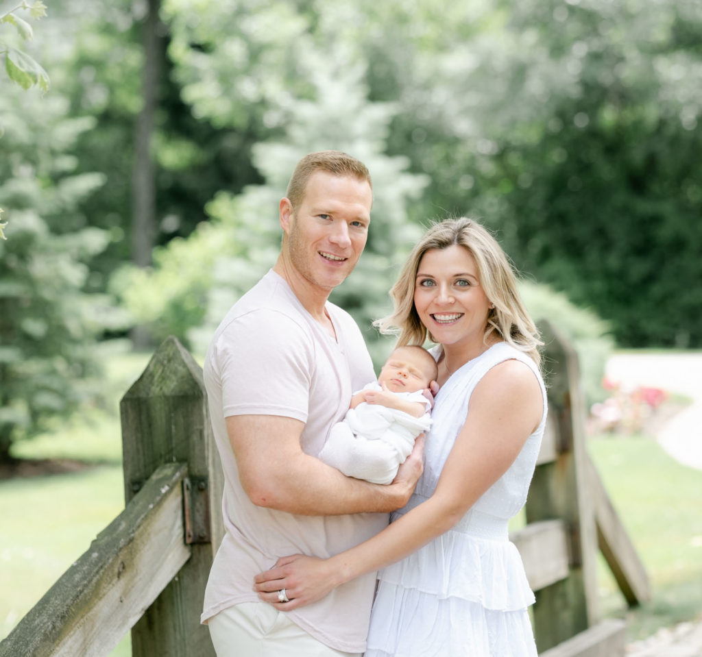 mom and  dad pose outdoors with their newborn  during their north shore family photographer session