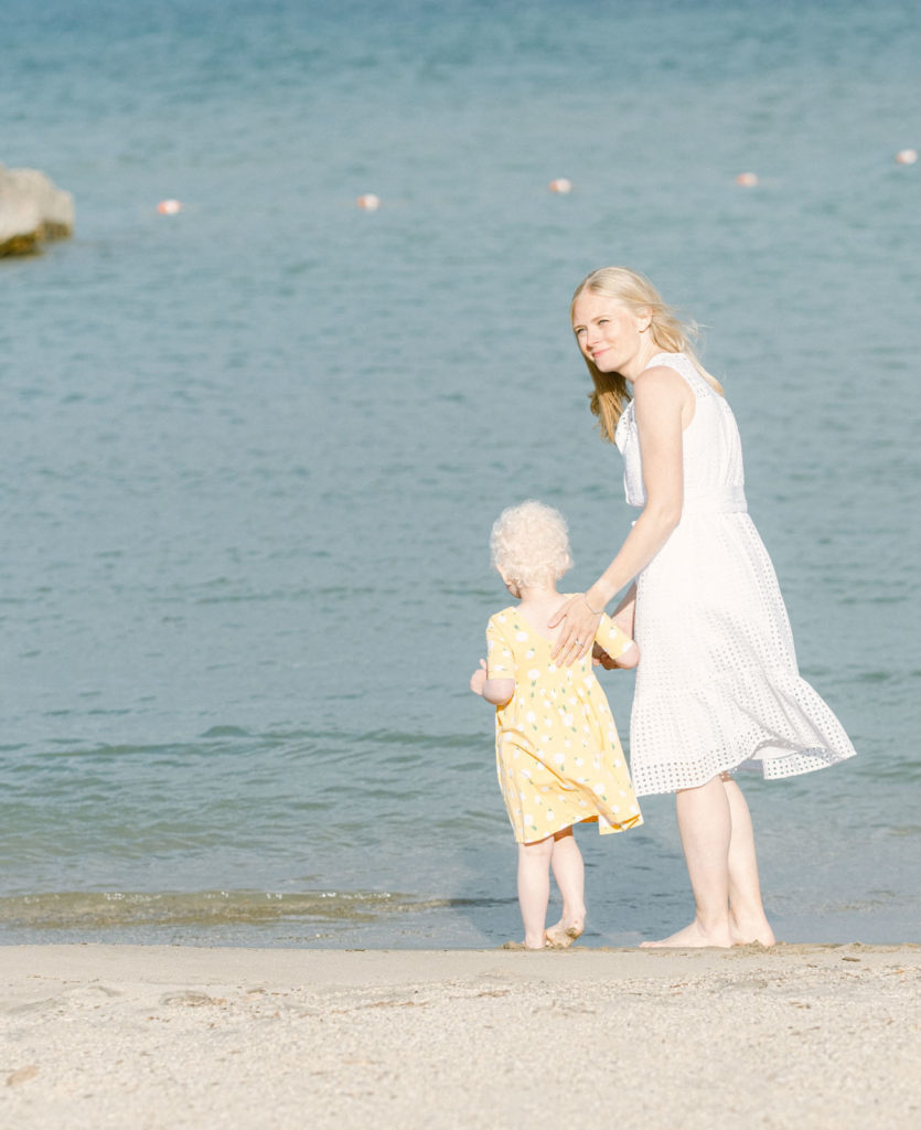 A mom holds her daughter's hand while looking back at her family on the beach