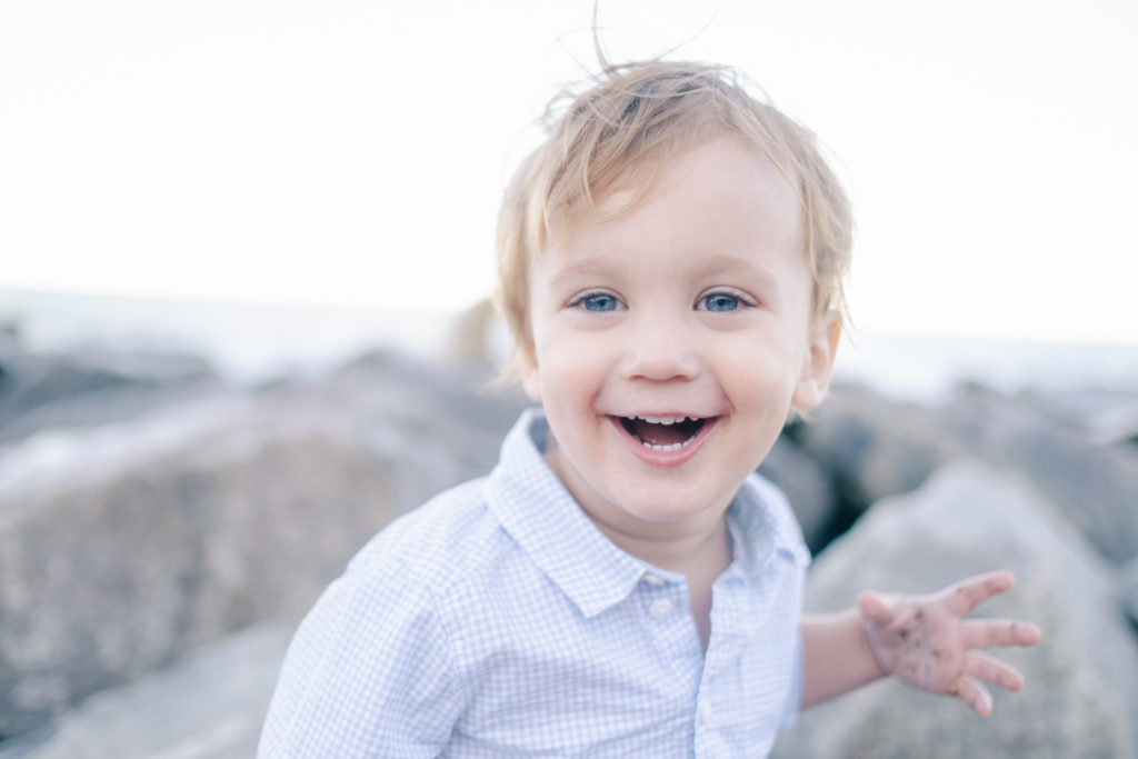 Close up of little boy with a big smile while he's sitting on the rocks at Lake Bluff beach