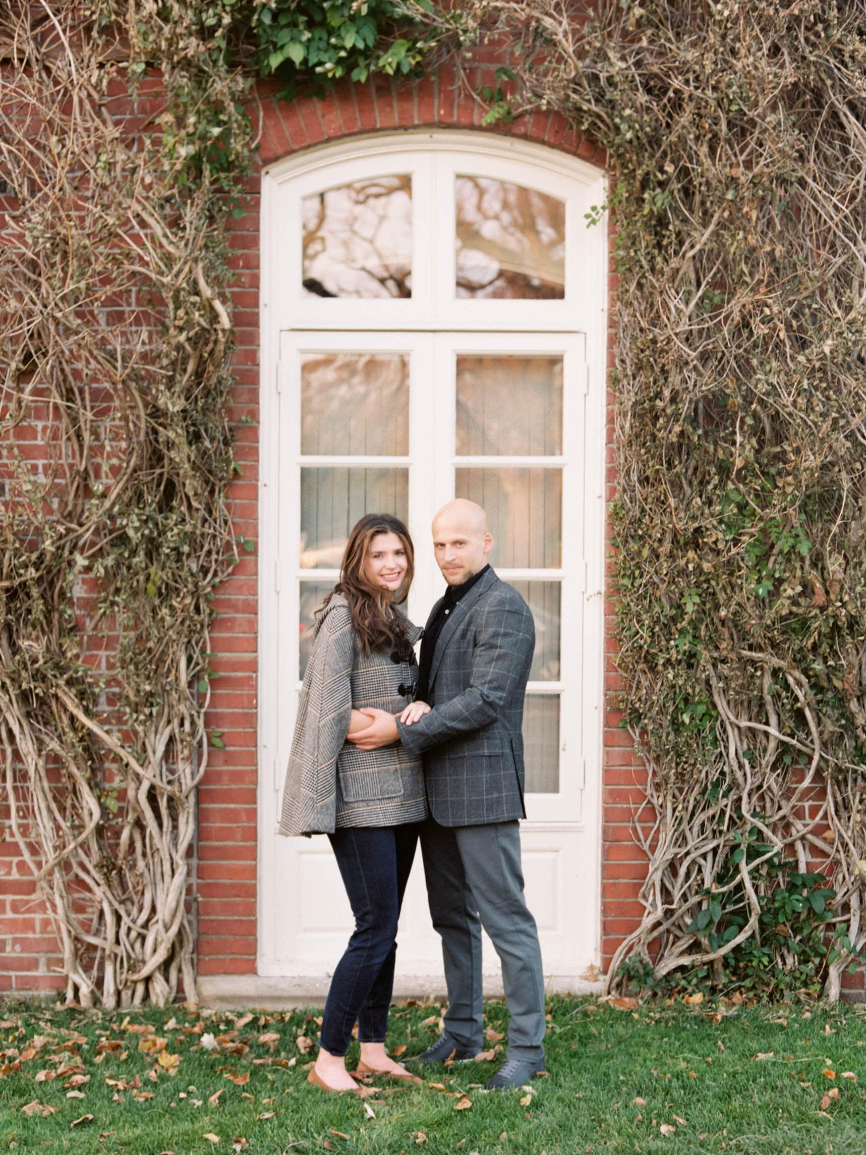 A couple embrace each other in front of a doorway covered in green vines