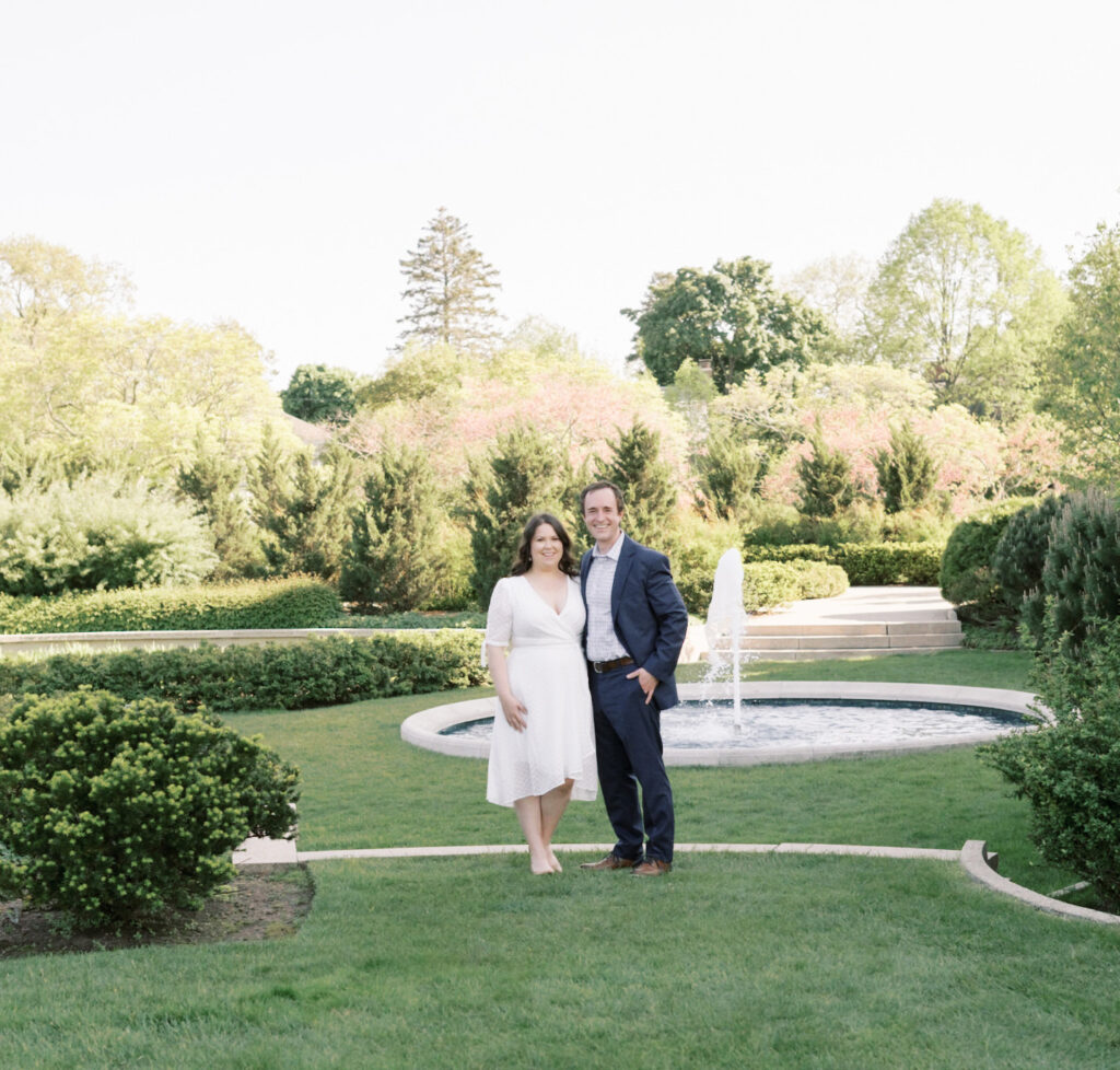 A recently engaged couple stand together in a garden setting