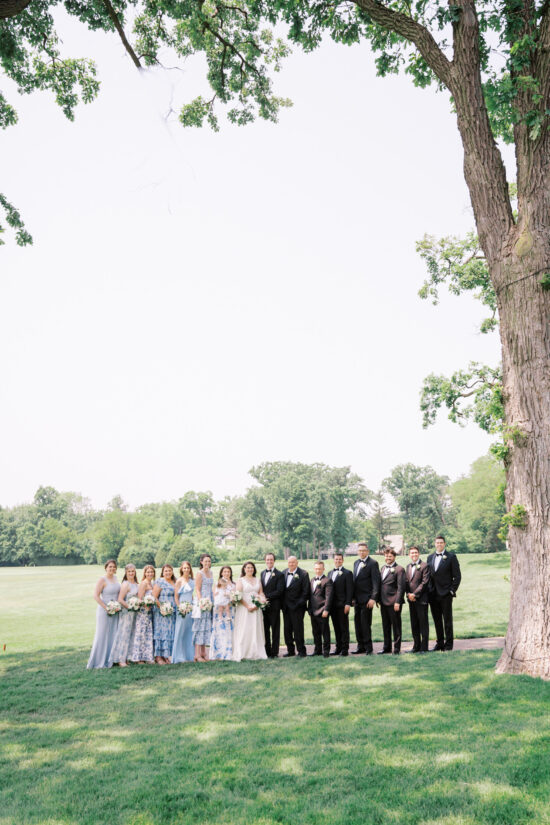 A large wedding party poses under a large Oak tree for formal portraits on the grounds of Highland Park's Exmoor Country Club.
