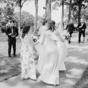 a bride walks along a path with her bridesmaids holding her dress