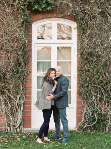 a couple poses in front of a white paned window surrounded by ivy